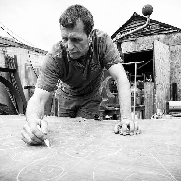Greyscale photo of Michael Jacques sketching a design in chalk onto a piece of board standing in front of the workshop